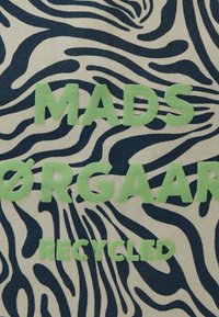 Tissu recyclé avec un fond beige et des rayures zèbre bleu marine, mis en valeur par un lettrage vert audacieux, "MADS ØRGAARD RECYCLED."