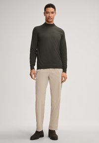 Dunkelgrüner Longsleeve-Pullover mit hohem Kragen, kombiniert mit hellbeigen Hosen, getragen mit braunen Knöchelstiefeln, einfarbige Textur.