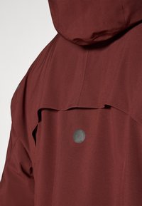 Rote wasserdichte Jacke mit Kapuze, strukturiertem Stoff und einer Vorderklappe mit silbernem Druckknopf-Detail.