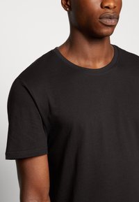 Schwarzes Baumwoll-T-Shirt mit rundem Ausschnitt und kurzen Ärmeln, das über eine glatte Textur und ein einfaches Design verfügt.