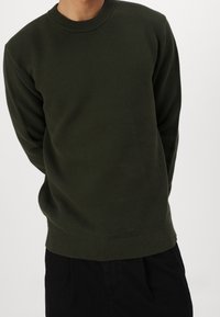 Grön stickad tröja med rund ribbad halsringning och långa ärmar. Har en strukturerad tyg och ribbad fåll och manschetter.