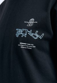 Černé tričko s modrými a bílými grafickými designy na hrudi, včetně textu a loga zeměkoule, vyrobené z bavlněné smíšeniny.