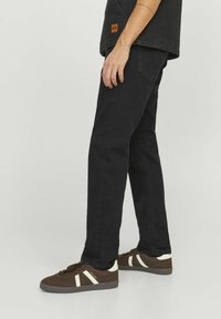Black denim jeans with a straight fit, featuring back pockets and side seams, paired with brown sneakers and white accents.