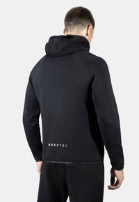 Sudadera negra con un diseño ajustado, que presenta una gran capucha, textura suave y "MOROTAI" impreso en la parte trasera, en el dobladillo.