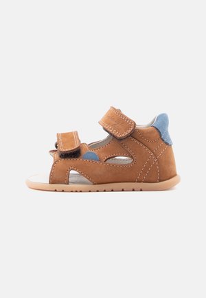 Brun børnesandal med to justerbare velcroremme og blå stofdetaljer på hæl og side, set fra siden.