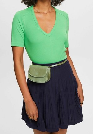 Haut vert côtelé à manches courtes avec un col en V, associé à une jupe plissée bleu marine. Un petit sac bandoulière vert clair est attaché à la taille.