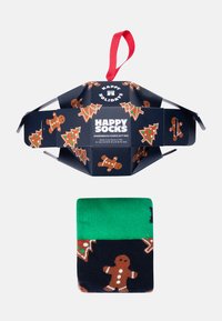 Caja de regalo de galletas de jengibre con papel negro que presenta hombres de jengibre y árboles de Navidad. Calcetines verdes y negros con patrones de jengibre.