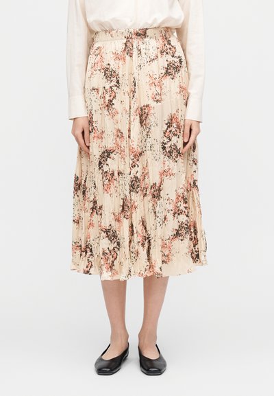 Woman wearing a cream blouse and a beige pleated midi skirt with pink and black floral print, paired with black flat shoes.
