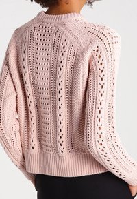 Pull en tricot rose avec un design ajouré, des rayures verticales texturées, des poignets côtelés et un col rond.