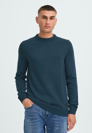 Dunkeltürkiser Strickpullover mit langen Ärmeln und rundem Ausschnitt, versehen mit einem strukturierten Muster und einem kleinen Logolabel am Saum.