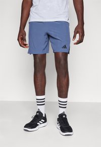 Blue athletic shorts with a black logo, paired with black sneakers and white striped socks. The shirt is gray and slightly textured.