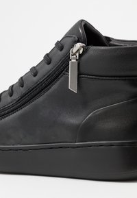 Chaussures noires en cuir à lacets plats, avec fermeture éclair sur le côté et semelle en caoutchouc texturée. Présente un tire-zipp en métal et une finition lisse.