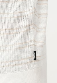 Tissu en maille blanche avec de fines rayures horizontales beige et une petite étiquette noire portant la mention "BOSS" près du bord inférieur.