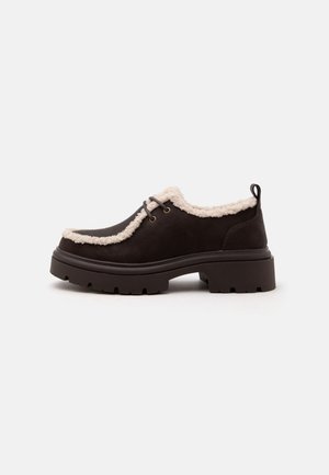 Chaussure marron foncé à lacets avec semelle épaisse et doublure en polaire crème le long du col et de la languette, vue de côté sur fond blanc.