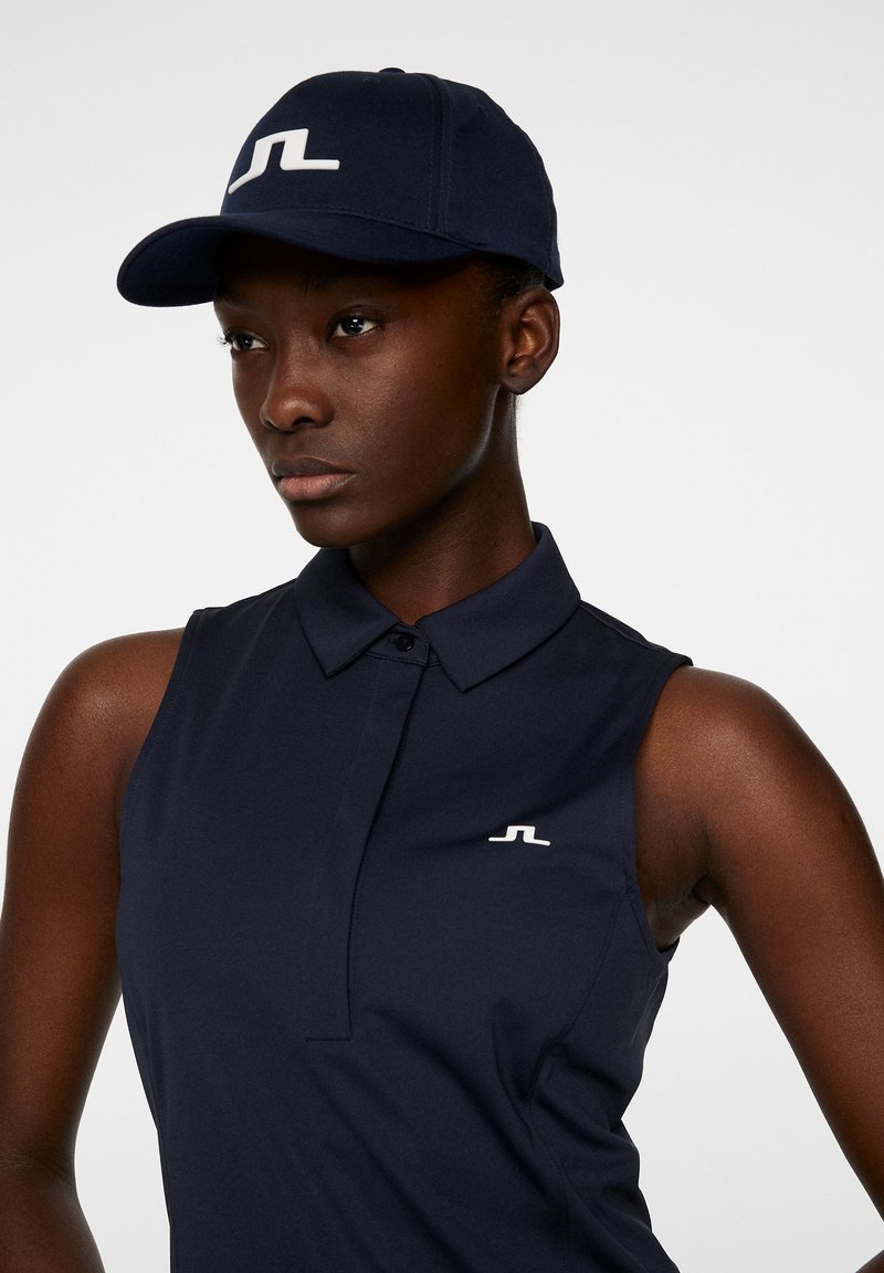 Polo senza maniche blu navy con colletto e logo bianco sul petto, abbinato a un cappellino blu navy con logo bianco.