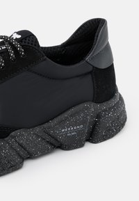 Close-up van een zwarte sneaker met mesh- en suède details, patroonveters en een gespikkelde, chunky zool met het label "WEEKEND MaxMara".