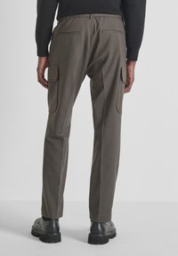 Pantaloni cargo in tessuto verde oliva, con vita elasticizzata, tasche cargo laterali e tasche a soffietto posteriori. Indossati con scarpe nere.