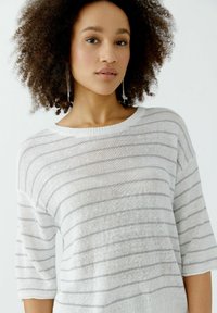 Leichtes weißes Strickpullover mit horizontalen grauen Streifen, weitem Bootsausschnitt und kurzen Ärmeln, mit einer weichen Textur und subtilen Glitzer.