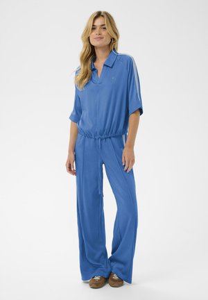 Modro kombinezo iz mehke tkanine z ovratnikom, kratkimi rokavi, elastiko v pasu in širokimi hlačnicami z belimi stranskimi črtami.