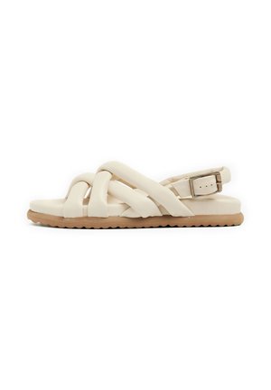 Light beige sandals with interwoven straps, adjustable ankle buckle, textured outsole, and flat sole design. Made from synthetic material.