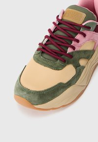 Zapatilla que combina materiales en tonos beige, verde y rosa. Parte superior sintética con detalles de ante y cordones burdeos. Suela de caucho.