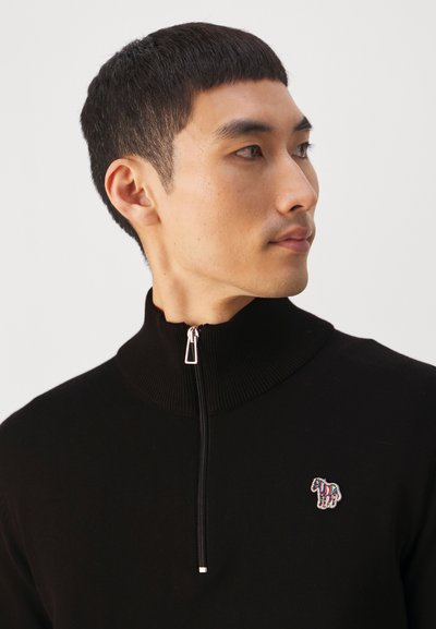 Fekete cipzáras pulóver magas gallérral, bal mellrészen színes hímzett állatlogóval és sima textúrával.