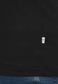 Black cotton t-shirt featuring a simple design. Notable details include a small white tag with an exclamation mark near the hem.