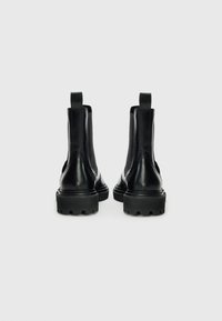 Bottines en cuir noir avec une finition texturée, des poignées de tirage et des semelles en caoutchouc épaisses avec des motifs de semelle prononcés.