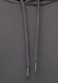 Närbild av grå huvtröjefabric med två grå dragsnören hängande ner, som visar textur och sömnadsdetaljer.