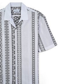 Camicia a maniche corte in tessuto leggero con vestibilità rilassata, caratterizzata da strisce verticali geometriche nere su fondo grigio chiaro e colletto bianco.