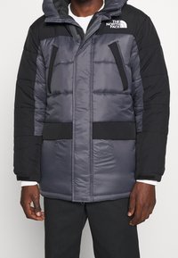 Pikowana kurtka parka w kolorze szarym i czarnym, z kapturem, zamkiem błyskawicznym, kieszeniami na piersi oraz miękką fakturą materiału. Marka na ramieniu.