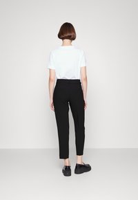 Pantalons noirs ajustés avec un design droit, associés à un t-shirt blanc uni. Le mannequin porte des chaussures noires ; style minimaliste.
