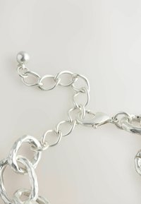 Sølv metal kæde med afrundede, strukturerede led og en poleret finish; inkluderer en lås og en glat, sfærisk accent.