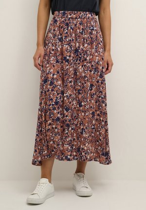 Luchtige midi-rok met bloemmotief in bruin, marineblauw en wit, gedragen met witte sneakers en een ingestopt zwart shirt.