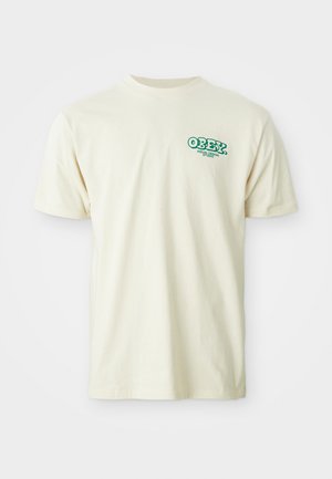 Krämfärgad bomulls-t-shirt med korta ärmar och rundad halsringning, med en grön "OBEY VISUAL DEBIR"-logotyp på övre vänstra bröstet.