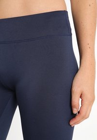 Granatowe legginsy sportowe o gładkiej fakturze i wysokim stanie. Widoczne szwy wzdłuż boków i w okolicy pasa.