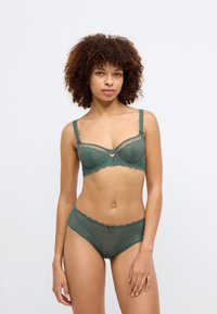 Πράσινο σετ δαντελένιου εσωρούχου που περιλαμβάνει σουτιέν με κυματιστές άκρες, ένα μικρό διακοσμητικό δαχτυλίδι και ταιριαστά ψηλόμεσα εσώρουχα με δαντελένια διακοσμητική λεπτομέρεια.