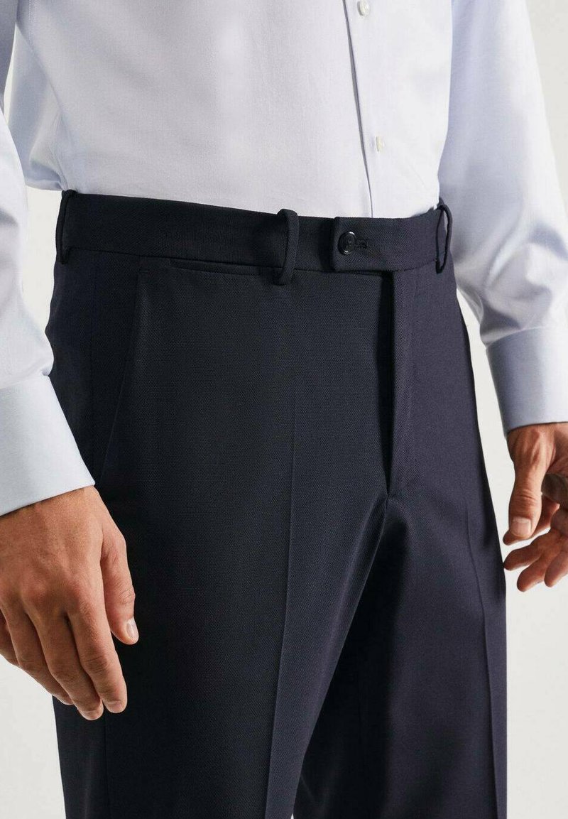 Pantalons navy en tissu lisse avec une ceinture et des boutonnières visibles, dotés de poches latérales et d'une coupe ajustée.