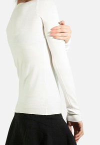 Un pull ajusté à manches longues blanc en maille lisse, avec un ourlet et des poignets côtelés, porté avec une jupe noire.