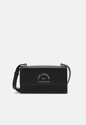 Czarna prostokątna torba na ramię z regulowanym paskiem i srebrnym napisem "Karl Lagerfeld Paris 21 Rue St-Guillaume" na klapie.