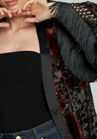 Kimono negru cu imprimeu floral și textură de catifea, având mâneci lungi cu franjuri și material transparent. Stilizat peste un top negru și pantaloni din denim.