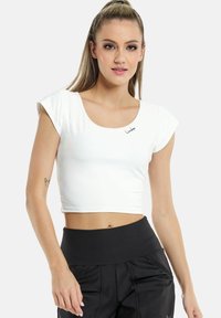 Hvid crop top med korte cap ærmer, en rund udskæring og lille sort logo på brystet, parret med højtaljede sorte bukser.