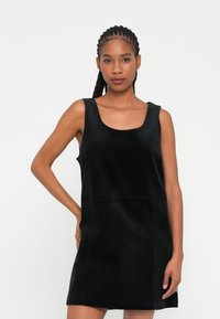 Rochie din catifea neagră cu decolteu în formă de semicerc și design fără mâneci, având o croială dreaptă și linii de textură verticale.