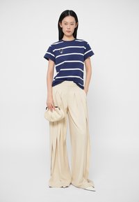 Camiseta de rayas marineras con franjas blancas y un pequeño diseño gráfico, combinada con pantalones anchos plisados color crema y un pequeño bolso de mano crema.