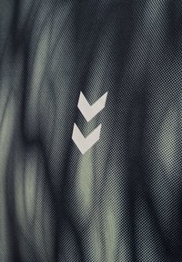 Svart och grönmönstrad tyg med en struktur av små prickar. Vitt chevronsymbol som är placerad framträdande på höger sida.