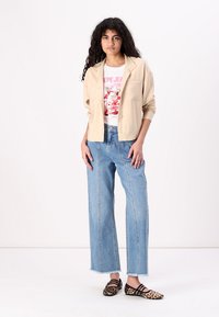 Beige cropped jacket over a white graphic t-shirt, paired with light blue wide-leg jeans and leopard print flat shoes.