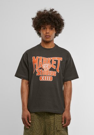 Mørk grå t-skjorte, oversized passform, med oransje grafisk tekst "MARKET Studios XIII" og en tigerillustrasjon på forsiden. Korte ermer.