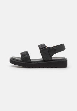 Schwarze, gesteppte Sandalen mit verstellbaren Riemen und goldfarbenen Beschlägen. Sie verfügen über eine dicke, strukturierte Plattformsohle für Halt und Komfort.
