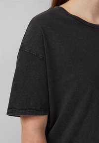 Zwarte t-shirt met een relaxte pasvorm, korte mouwen en een lichtgestestructureerde stof. De halslijn is rond, met zichtbare stikseldetails.