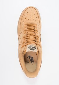 Nike Air Force 1 sneakerit ruskeassa mokassa, pyöreällä kärjellä, rei'itetty yläosa, nauhakiristys ja vaaleanbeige kumipohja. Sisätiloissa näkyvä brändäys.